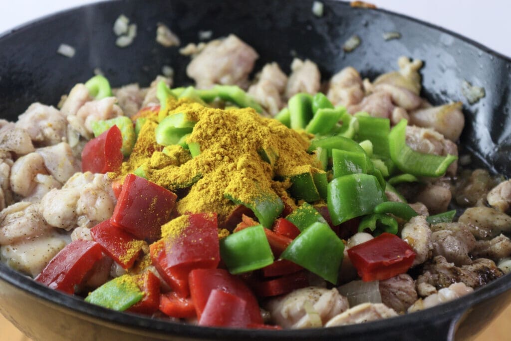 Image showing how to add chicken thighs, bell peppers, spices and curry powder to the pan